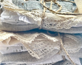 May include: A stack of assorted fabric scraps, including white, cream, and light blue lace and linen. The fabrics are tied together with twine. The image shows a variety of textures and patterns, perfect for crafting or textile projects.