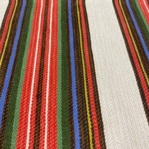 May include: A white fabric with red, green, blue, brown, and yellow stripes. The fabric has a woven texture.