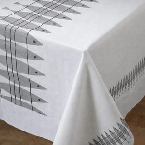 May include: White tablecloth with a repeating pattern of gray fish. The fish are arranged in rows, with black vertical lines and small black dots representing eyes. The tablecloth is made of a light-colored fabric.