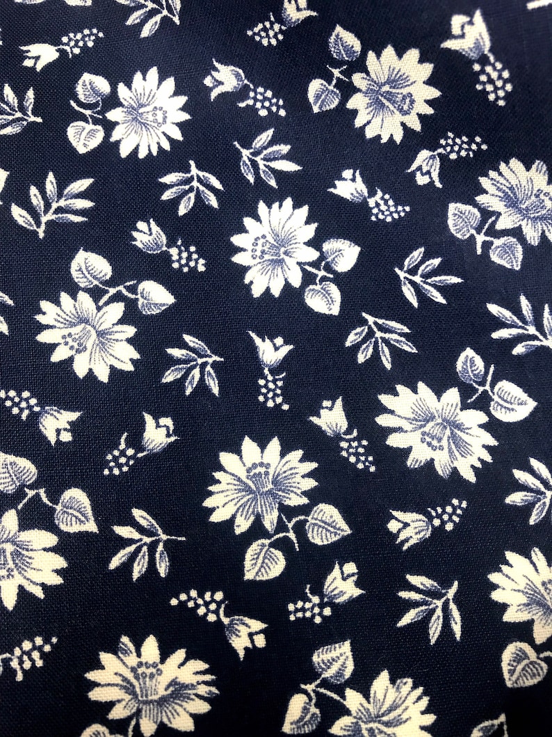 Puede incluir: Una tela azul marino con un patr&oacute;n floral blanco. El patr&oacute;n presenta peque&ntilde;as flores blancas, hojas y bayas.