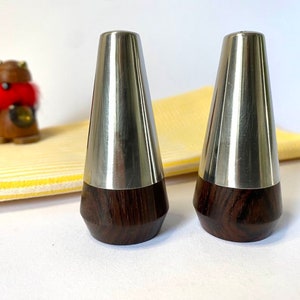 Pode incluir: Um conjunto de dois saleiros e pimenteiros de prata com bases de madeira escura. Os saleiros são em forma de cone e têm um acabamento polido.