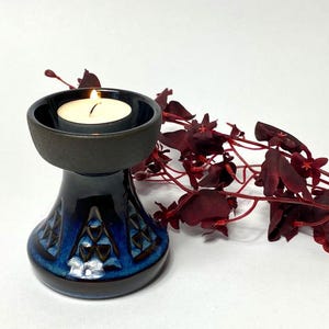 Könnte beinhalten: Ein blauer und brauner Kerzenhalter aus Keramik mit geometrischem Muster. Eine weiße Teelichtkerze brennt im Halter.