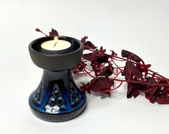 May include: A blue and brown ceramic candle holder with a geometric design. A white tea light candle is burning in the holder.