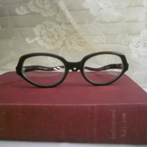 May include: Black plastic framed glasses with a red book in the background. The book has the text "Authorized Edition" on the spine.