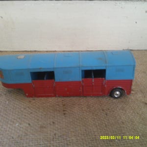 May include: A blue and red toy horse trailer with three stalls. The trailer has a blue roof and red sides with three separate stalls.