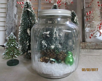 Vintage Hoosier Jar with Bottle Brush Tree and Pine combs and Green Ornaments, Collection of Vintage Christmas Decorations sitting in snow.