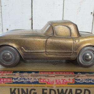 Könnte beinhalten: Ein goldfarbenes Spielzeugauto aus Metall in Form eines Chevrolet Corvette. Das Auto ist ein Vintage-Spielzeug und hat einen Schlitz im Heck für Münzen.