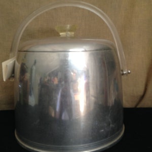 Puede incluir: Un cubo de hielo plateado con un asa de plástico transparente y una tapa de plástico amarilla.