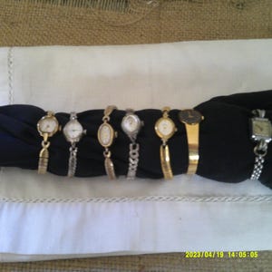 May include: A collection of vintage wristwatches, each with a unique design. The watches feature gold and silver bands, and various face shapes, including round and oval. The watches are displayed on a black surface, set against a white cloth.