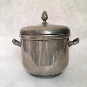 Puede incluir: Un azucarero de plata con tapa y dos asas. La tapa tiene un pequeño pomo decorativo en la parte superior.