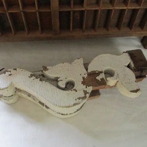 May include: Two white painted wooden corbels with intricate scrollwork designs. The corbels are stacked on top of each other and have a distressed, aged look.