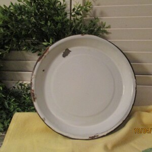 May include: White enamel pie plate with a black rim and rust spots around the edge.