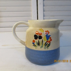 May include: A vintage ceramic pitcher with a blue and white glaze. The pitcher features a floral design with red, yellow, blue, and black flowers.
