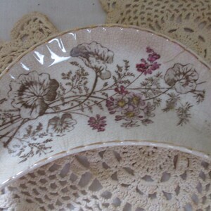May include: A white ceramic half-moon shaped dish with a floral design in brown and pink. The dish has a gold rim.