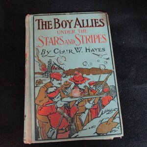 Op de afbeelding: Vintage boek getiteld "The Boy Allies Under the Stars and Stripes" van Clair W. Hayes. De omslag toont een illustratie van soldaten in rode uniformen, tegen een lichtblauwe achtergrond, met de titel in rood en zwart.
