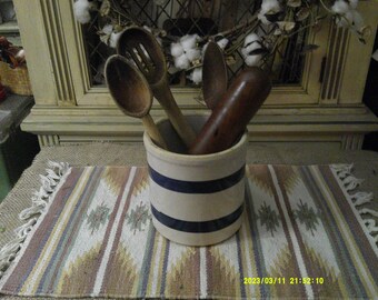 Puede incluir: Un porta utensilios de cerámica blanca con rayas azules, lleno de cucharas de madera y un rodillo de madera.