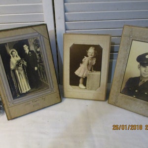 Può includere: Tre fotografie d'epoca incorniciate. La prima foto mostra una coppia di sposi in abiti formali. La seconda foto mostra una bambina con un vestito rosa. La terza foto mostra un uomo in uniforme militare.