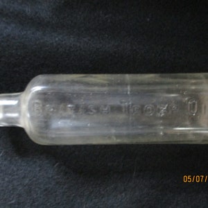 Puede incluir: Una botella de vidrio transparente con fondo redondeado y cuerpo largo y rectangular. La botella tiene una pequeña abertura en la parte superior y una etiqueta que dice "FRESH 10 OZ".