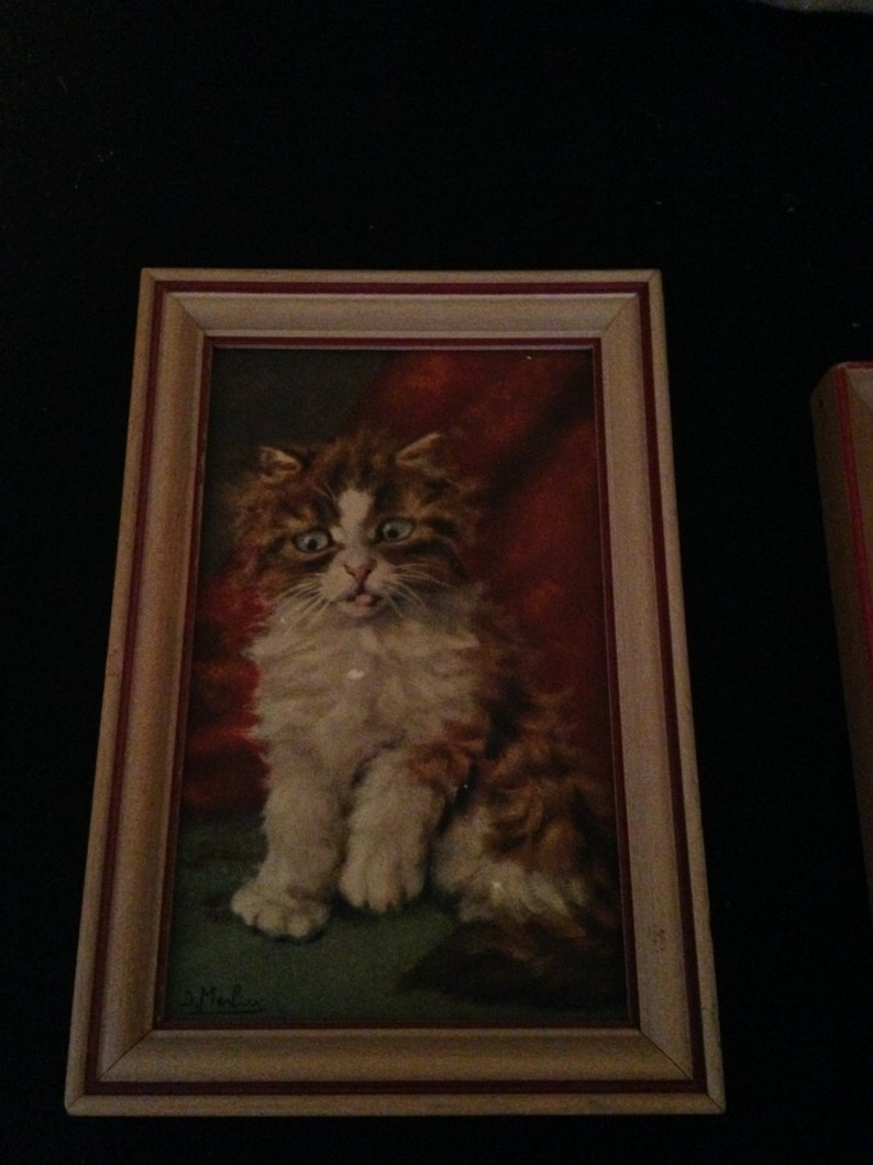 May include: A framed painting of a fluffy cat with ginger and white fur, set against a red backdrop. The cat is depicted in a seated position with a slightly open mouth. The frame is light brown with a red inner border.