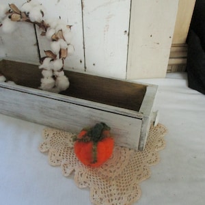 以下が含まれることがあります： 白いペンキで塗られた木製のプランターボックスで、内側は茶色です。プランターには、綿のリースと小さなオレンジ色のフェルトの南瓜が入っています。