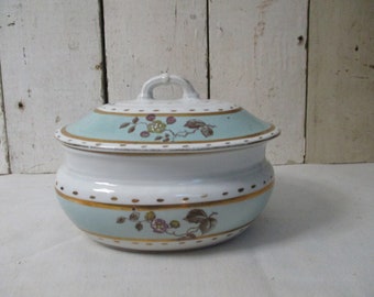 May include: A white ceramic oval-shaped dish with a lid. The dish has a blue and gold trim with a floral design. The lid has a knob on top.