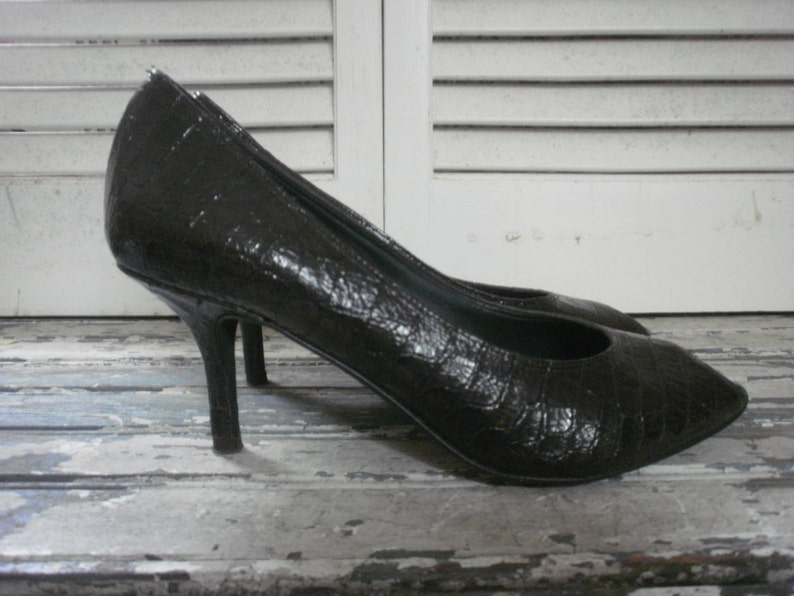 May include: A pair of black high-heeled shoes with a textured, reptile-like pattern. The shoes have pointed toes and slender heels. The heels are approximately 3 inches tall.