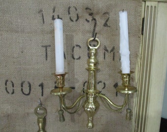 Könnte beinhalten: Goldfarbener Wand-Kerzenhalter mit drei Armen und drei weißen Kerzen. Der Halter hat ein dekoratives Design und ist aus Metall.