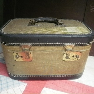 May include: A vintage tan and black travel case with brass hardware and a stitched design. The case has a black leather handle and a black leather trim around the edges.