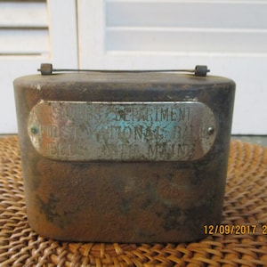 May include: A vintage metal money box with a silver plaque that reads "Savings Department First National Bank Belfast Maine".