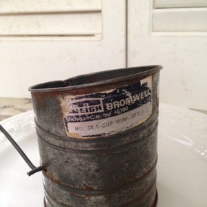 Op de afbeelding: Een vintage metalen 1-kops mini zeef met een zwart-wit label met de tekst "Eigh Brownwell Michigan City, Ind. 46360 No. 38 1-Cup Mini Sifter".
