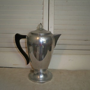 Puede incluir: Una cafetera de percolación de plata con un mango negro y una tapa de vidrio.