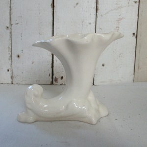 Può includere: Vaso in ceramica bianca con un'apertura a forma di tromba e una base ricurva.