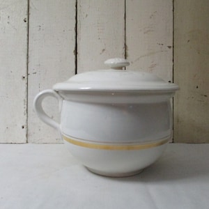 Op de afbeelding: Witte keramische pot met een deksel en een gouden band rond de rand. De pot heeft een handvat aan de zijkant.