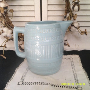 May include: A light blue ceramic jug with a barrel design. The jug has a handle and a spout.