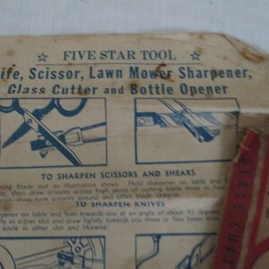 May include: Close-up of a vintage Five Star Tool sharpener with instructions on how to sharpen scissors, shears, knives, and lawn mower blades. The tool is made of metal and has a blue and white design.