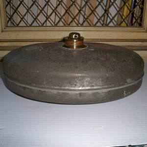 May include: A vintage, round, metal container with a brass lid. The container is grey and has a slightly textured surface.