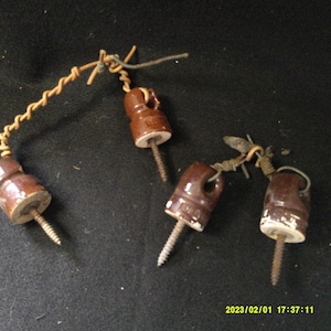 May include: Four brown ceramic electrical insulators with screw threads and wire attached. The insulators are on a black surface.