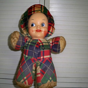 May include: A vintage plush doll with a plaid outfit and a smiling face. The doll has blue eyes and rosy cheeks.