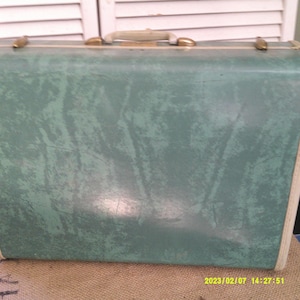 Könnte beinhalten: Ein vintage grüner Koffer mit weißen Verzierungen und goldenen Akzenten. Der Koffer hat ein strukturiertes, marmoriertes Muster.