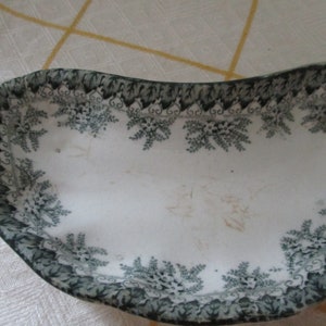 Puede incluir: Un plato de servir de cerámica blanca con un patrón floral verde alrededor del borde. El plato tiene forma de media luna.
