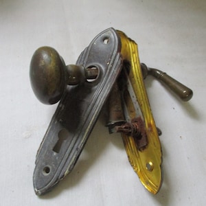 May include: Antique brass door hardware set with a round knob, a lever handle, and two decorative plates. The plates have a gold trim and a keyhole.