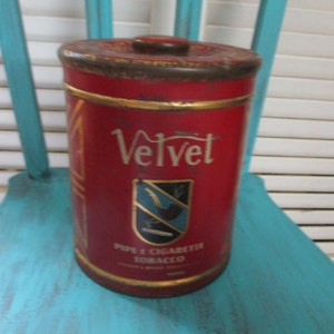 May include: A vintage red tin with gold trim and a gold rooster logo. The tin is labeled "Velvet Pipe & Cigarette Tobacco".