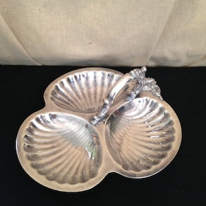 May include: A silver three-section serving dish shaped like seashells with a decorative handle.