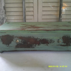 May include: A small wooden box with a single drawer painted in a distressed green and brown finish. The drawer has two small metal knobs.