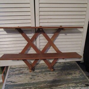 May include: A wooden wall shelf with two shelves and a criss-cross design. The shelf is made of brown wood and has a rustic look.