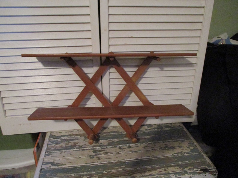 May include: A wooden wall shelf with two shelves and a criss-cross design. The shelf is made of brown wood and has a rustic look.