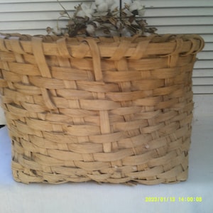May include: A woven basket made of natural materials, with a light brown color and a rectangular shape. The basket is empty and has a simple design.