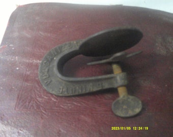 May include: A vintage metal clamp with a black finish. The clamp has a screw with a round knob and the words "Ideal" and "Caliper" are visible on the clamp.