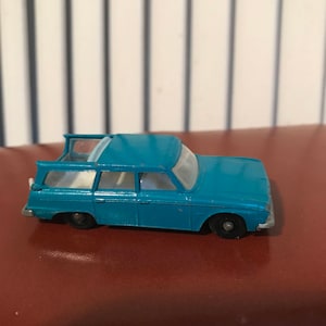 Könnte beinhalten: Ein blaues Spielzeugauto mit weißem Dach und weißem Innenraum. Das Auto ist ein Kombi mit einem Heckfenster und einer Heckklappe. Das Auto steht auf einer braunen Oberfläche.