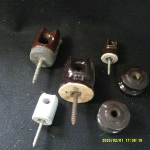 Könnte beinhalten: Fünf elektrische Isolatoren aus Keramik mit Gewindeschrauben aus Metall. Die Isolatoren sind braun und weiß und haben unterschiedliche Formen und Größen.